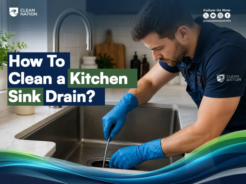 How to Clean a Kitchen Sink Drain? Professional cleaner wearing blue gloves uses a drain cleaning tool to remove debris from a modern stainless steel kitchen sink, demonstrating an effective method for unclogging and cleaning a kitchen sink drain.